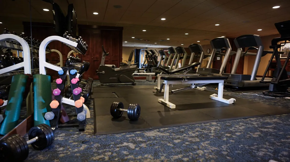 The energetic interior of the exercise facility features a full set of dumbbells, modern exercise machines, and a weight bench. Bright lighting and clean equipment create an inviting space for fitness enthusiasts.