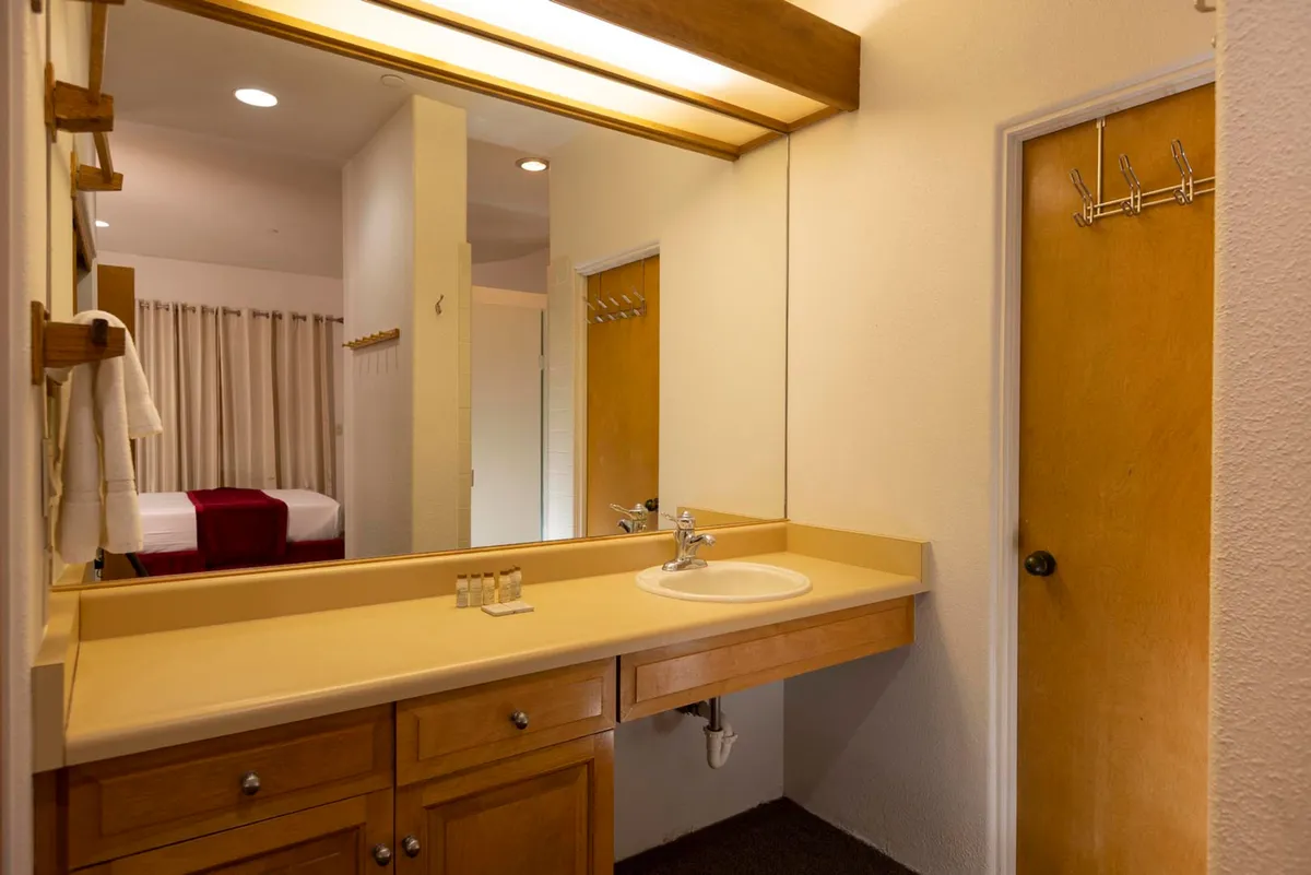 A serene ensuite area with a spacious sink, mirror, wooden cabinetry, and a towel rack, bathed in gentle morning light. The setting feels tranquil, ideal for personal grooming and quiet moments of self-care.