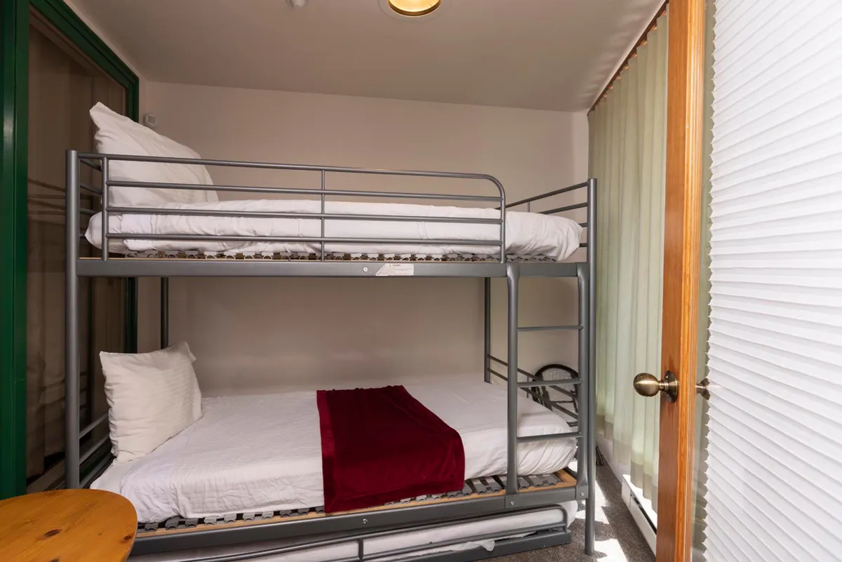 A welcoming space with bunk beds featuring a bold red blanket, a wooden table perfect for sharing moments, and plenty of natural light. The room radiates a casual, inviting vibe that encourages relaxation and connection.